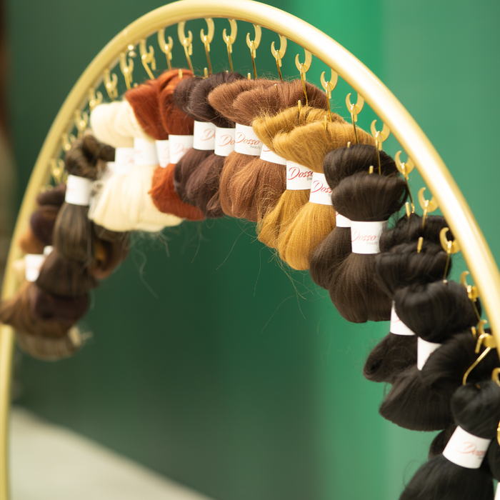 Assorted hair extensions hanging on a decorative stand against a green background