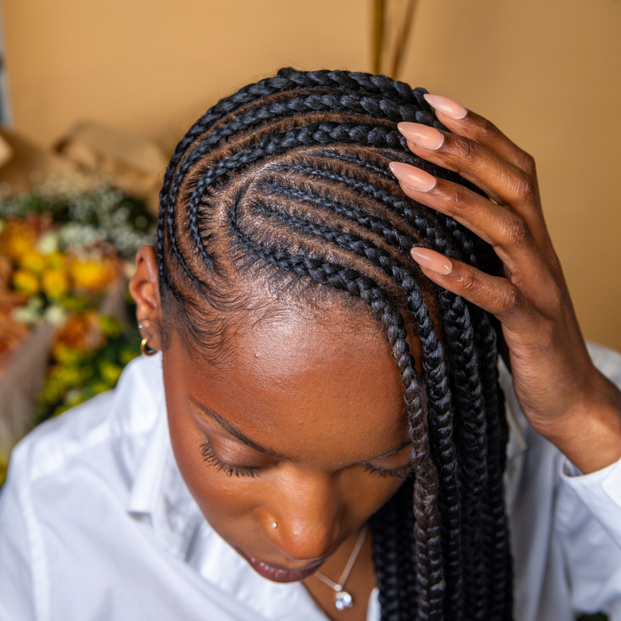 Person with braided hair touching their head, with a blurred brown background of a bouquet