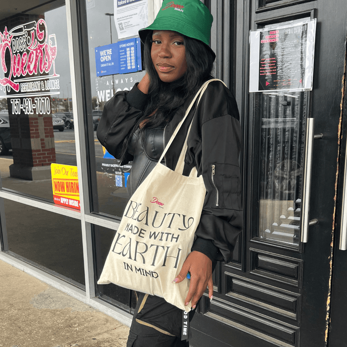 Woman wearing Dosso Beauty green bucket hat and carrying canvas tote bag with “Beauty Made With Earth in Mind” text outdoors