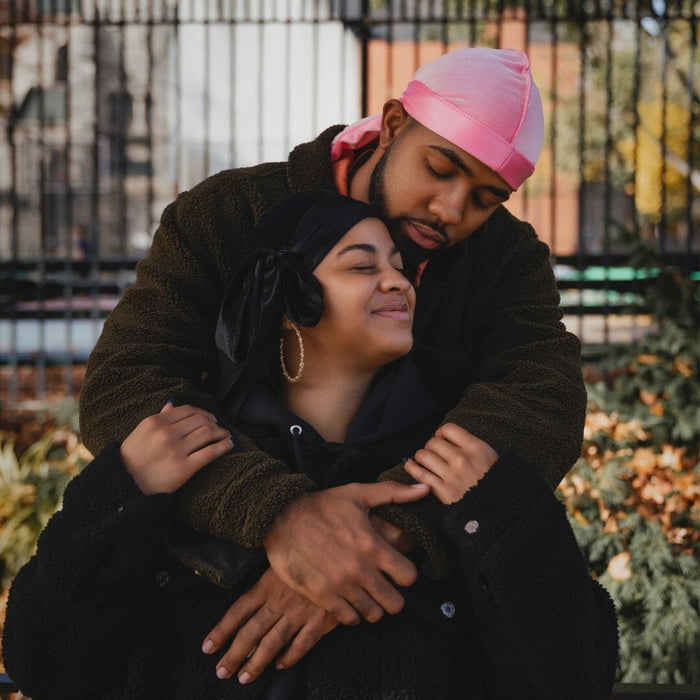 Couple wearing Dosso Beauty satin durags in pink and black embracing outdoors, showcasing protective hairwear and comfort