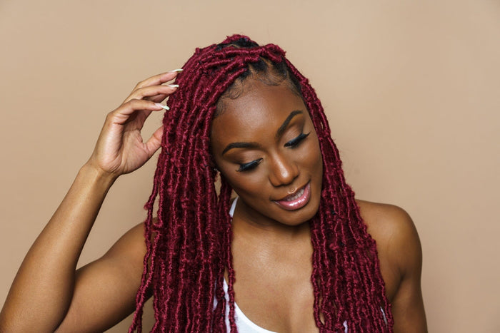 Woman adjusting red soft locs hairstyle, showcasing defined texture, length, and protective styling