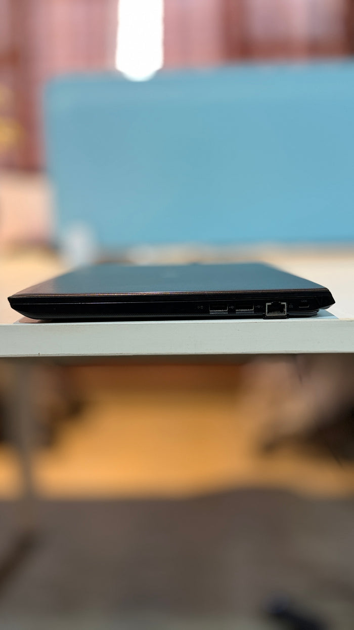 A black laptop shown from the side, resting on a white table with a heavily blurred indoor background.